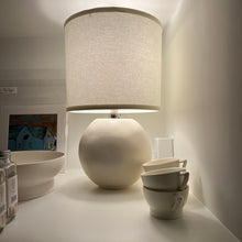 Load image into Gallery viewer, cream table lamp next to four coffee mugs, a bowl, and a unique piece of art