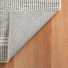 Load image into Gallery viewer, corner of the grey rug flipped up on hardwood floors