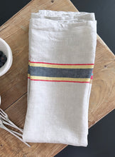 Load image into Gallery viewer, cream libeco tea towel with red, yellow, and black stripes in the center on a wooden board
