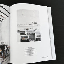 Load image into Gallery viewer, Curate book opened to a page showing home decor, kitchen with lights and a shelf with dishware, counter with open shelving below