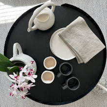 Load image into Gallery viewer, white plates on a balck table with mugs, a teapot, and a flower