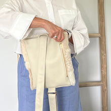 Load image into Gallery viewer, Model holding the back of the beige sheepskin bag and using the zipper