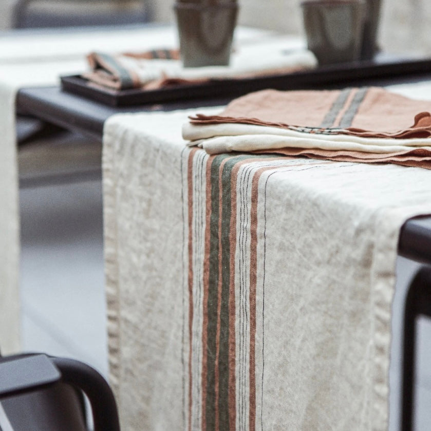 cream libeco table runner with red and grey stripes placed on a table with tea towels on top of it