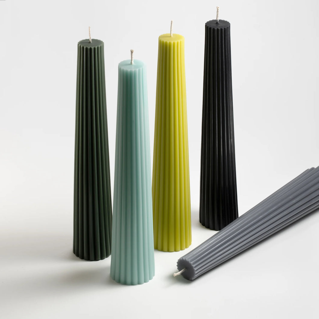 five pillar candles in shades of green and black standing in a line with one laying down in front