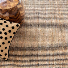 Load image into Gallery viewer, close up of the black and wicker rug pattern with a pillow and wooden side table 
