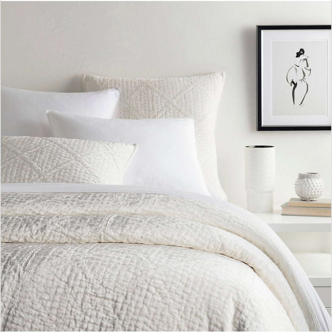 dove white velvet quilt on a white bed with a bedside table and art
