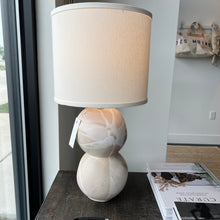 Load image into Gallery viewer, Stone earthy toned table lamp with a white lamp shade on a wooden table next to coffee table books
