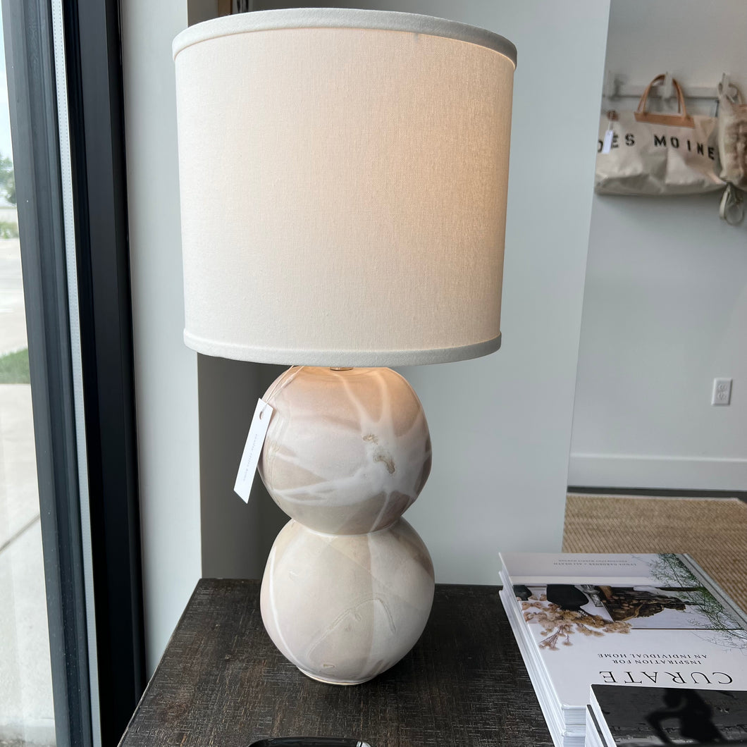 Stone earthy toned table lamp with a white lamp shade on a wooden table next to coffee table books