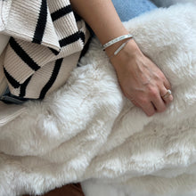 Load image into Gallery viewer, Model with a bracelet on holding the white throw on their lap

