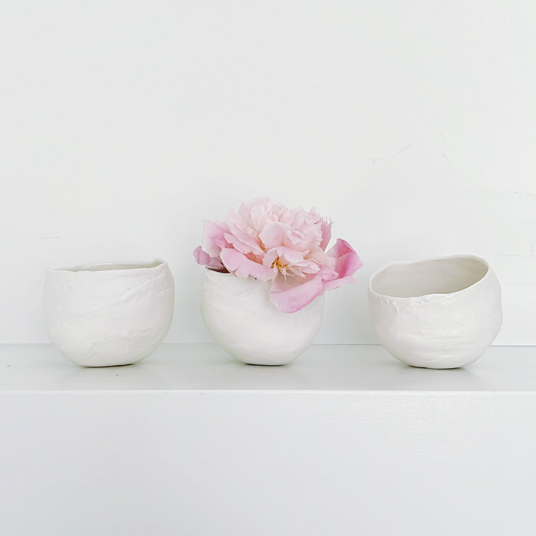 three plaster bowls on a shelf with one pink flower in the middle one