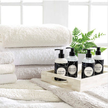 Load image into Gallery viewer, A pile of white bath rugs with bath towels and soap on to of the rugs
