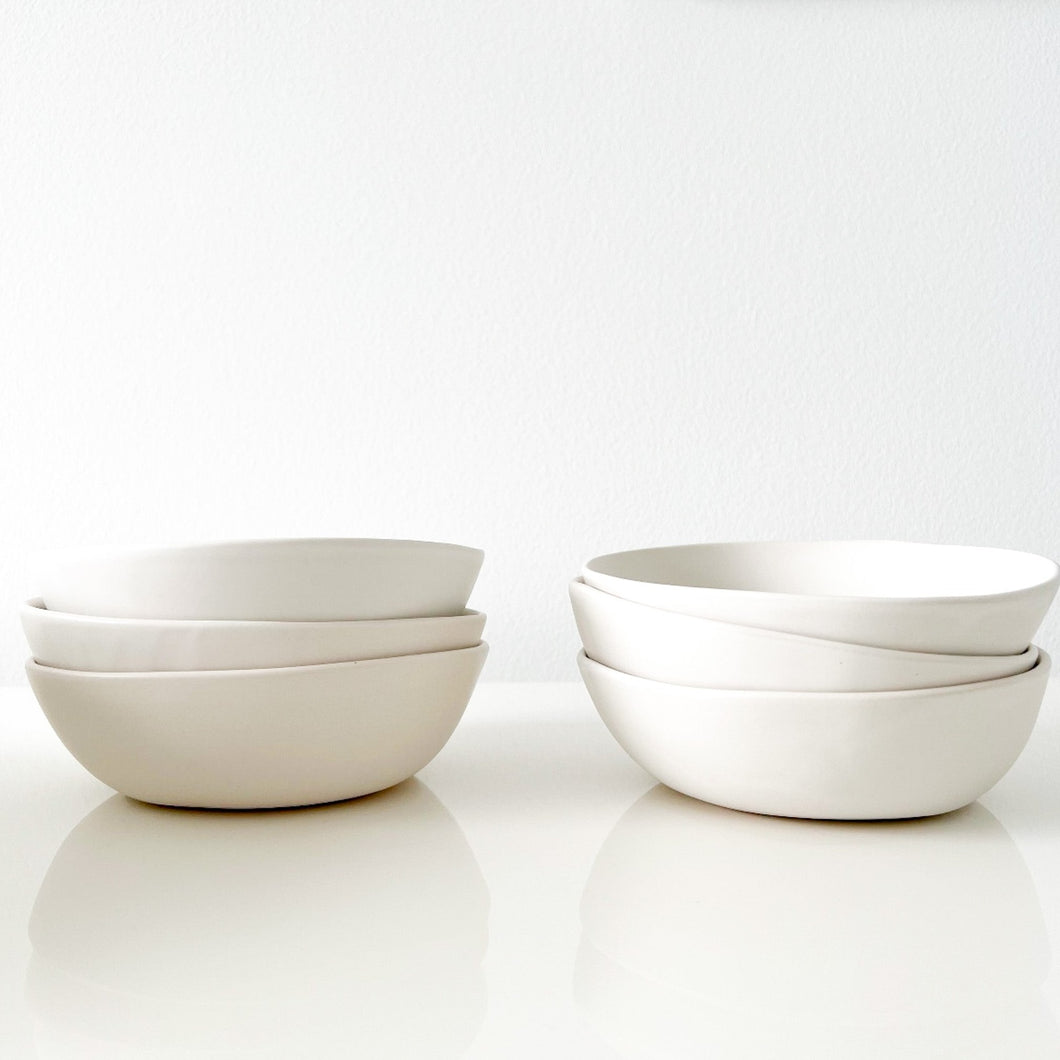 Two stacks of three white Alex Marhsall bowls on a white surface