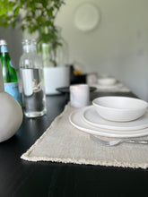 Load image into Gallery viewer, dining room table with placesetting in foreground and plant in background
