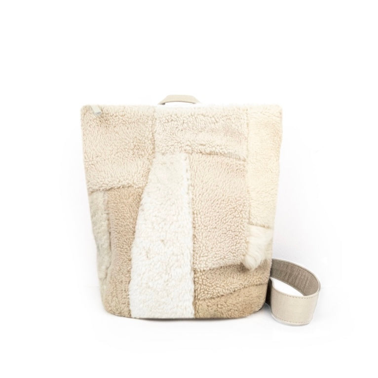 Beige pacthy sheepskin sling bag on a white surface