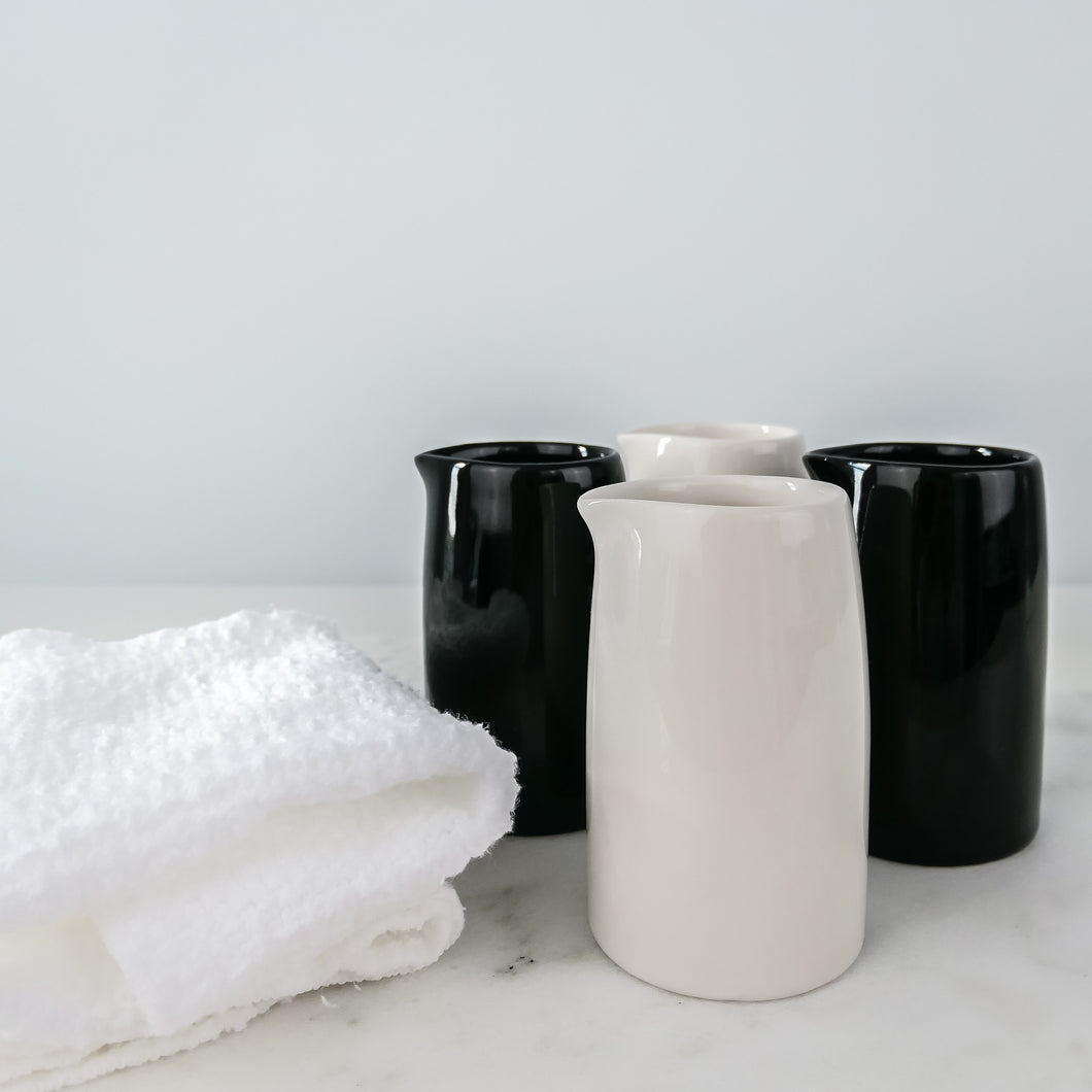 two white and two black milk jugs on a marble table