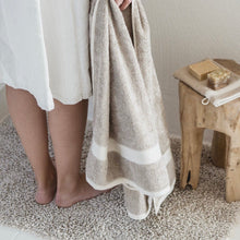 Load image into Gallery viewer, model holding a towel standing on an oatmeal colored libeco bath rug
