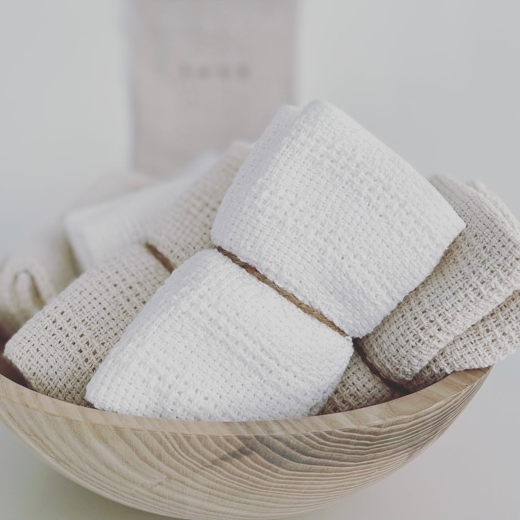 cotton washcloths wrapped in twine in a wooden bowl on a white counter 