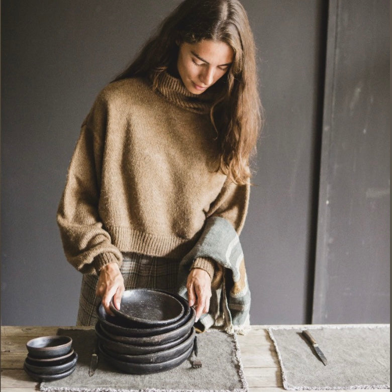 model holding a stack of black plates on the libeco place mat