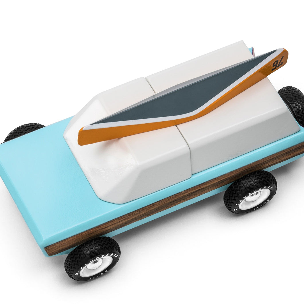 A toy sport utility truck painted blue and white shown from above.  It has a gray and orange canoe on top and a black spare tire on the back.