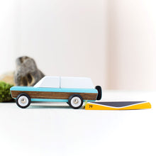 Load image into Gallery viewer, A wooden toy sport utility vehicle paitned blue and white and brown with a wooden toy canoe laying upside down behind the truck.  Pretend boulders can be seen in the background. 
