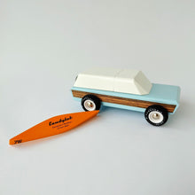 Load image into Gallery viewer, A wooden toy painted blue and white of a sport utility vehicle with woodgrain sticker on side and an orance canoe laying upside down next to it.
