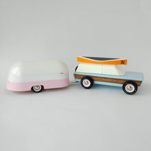 Load image into Gallery viewer, A blue and woodgrain toy car with an orance wooden canoe on top towing a pink and white camper, all from CandyLab.

