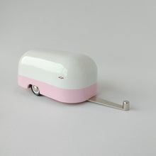 Load image into Gallery viewer, White and pink toy retro camper with black tires and a small image of a piece of candy on the front corner of the camper. 
