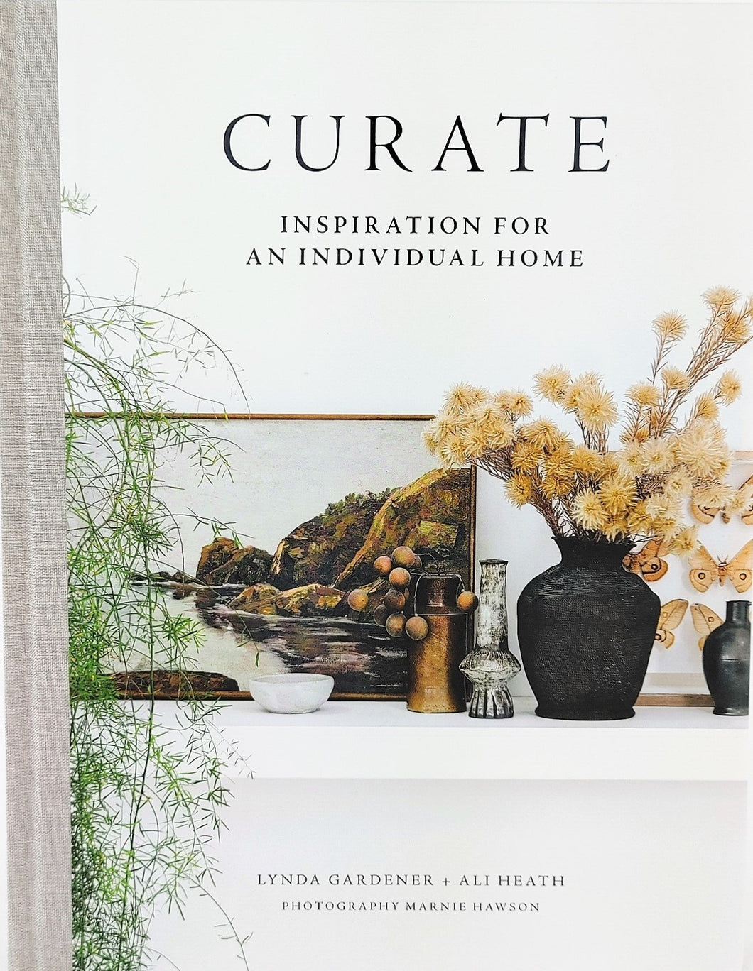 Front cover of book titled Curate, Cover has artwork, vases, vase with flowers, sitting on a mantle with green plant on side.