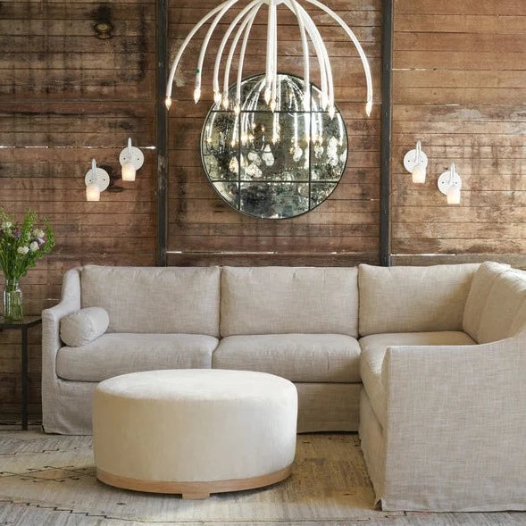 Beautiful sectional couch with a white ottoman, a wooden wall behind the couch, and a mirror centered on the wall 