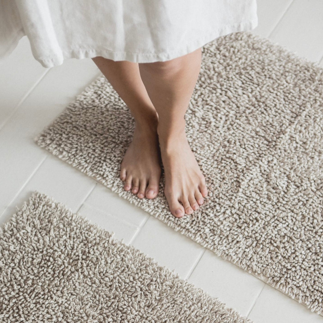 libeco oatmeal colored bath rug with a model standing on it
