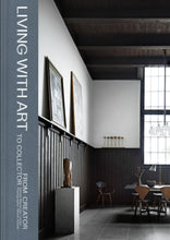 Load image into Gallery viewer, Front cover of book showing title &quot;Living With Art From Creator to Collector&quot;, and a photo of a room with art on a narrow shelf, a vase on a square stand, and a table with chairs.
