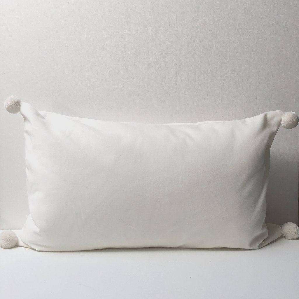 white pillow with pom poms on a white table